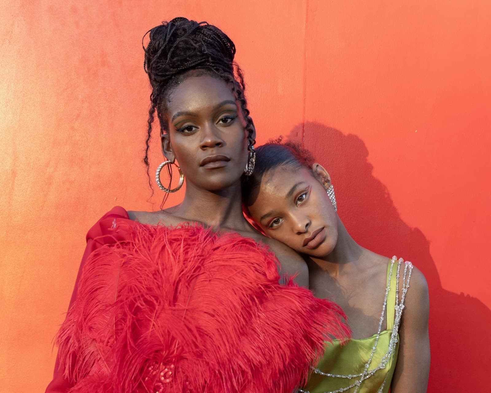 Two friends leaning on each other against a red wall